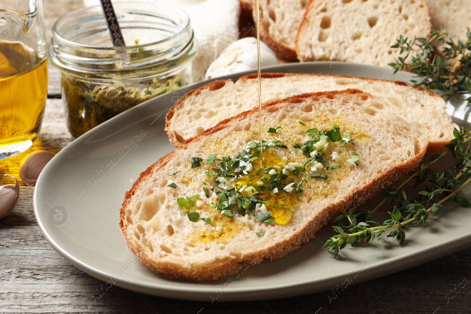 Photo of Pouring oil onto tasty bruschetta with garlic on wooden table, closeup