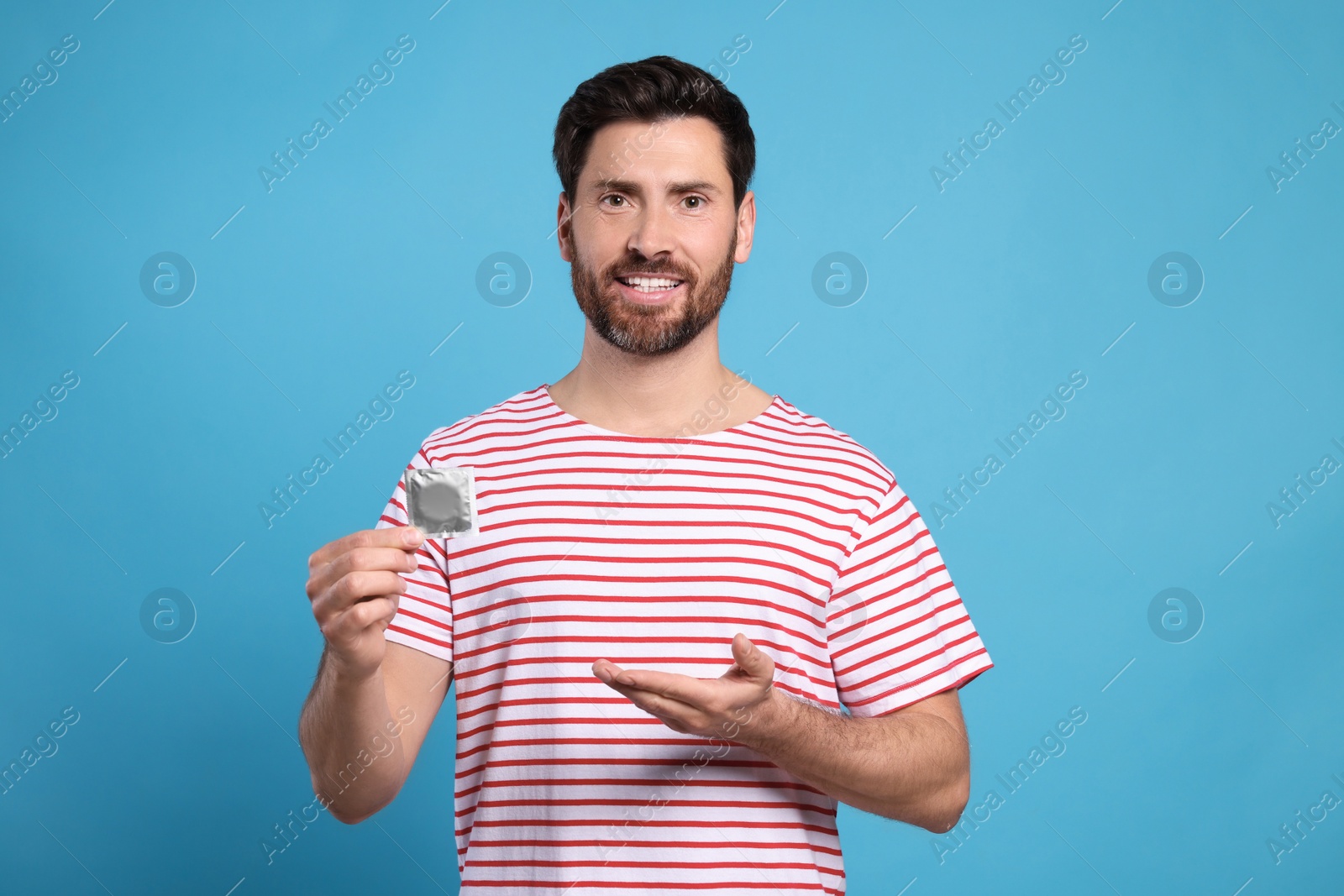 Photo of Happy man holding condom on light blue background. Safe sex