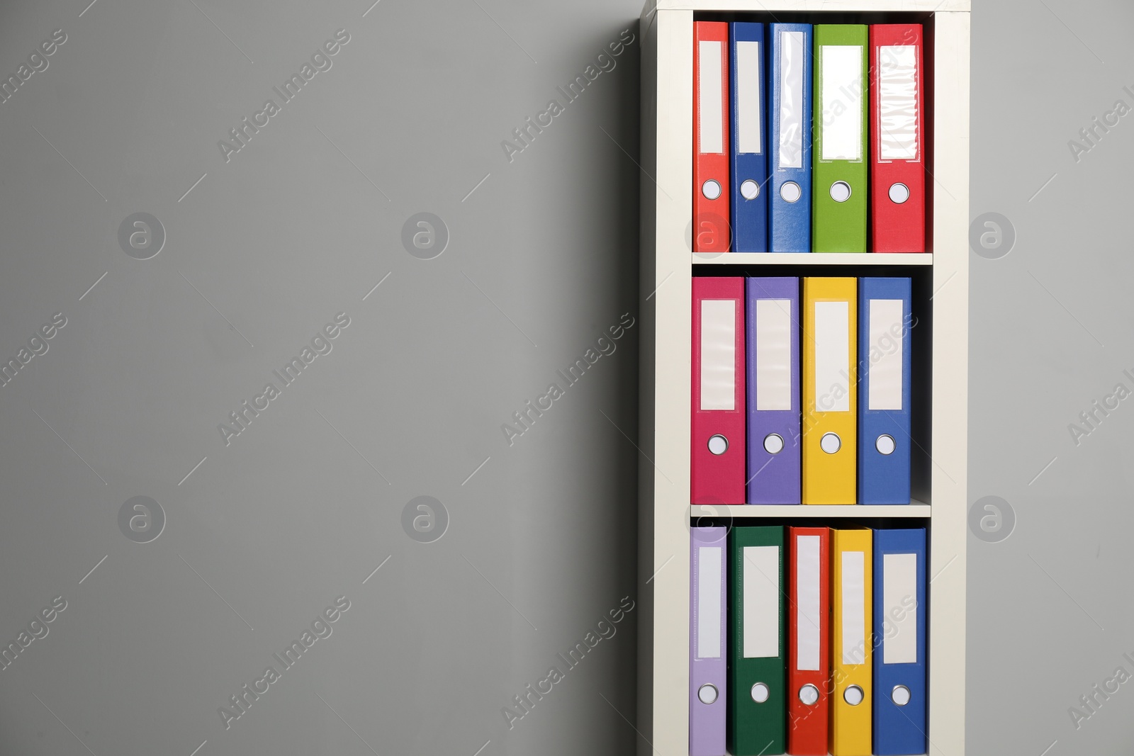 Photo of Colorful binder office folders on shelving unit near light grey wall. Space for text