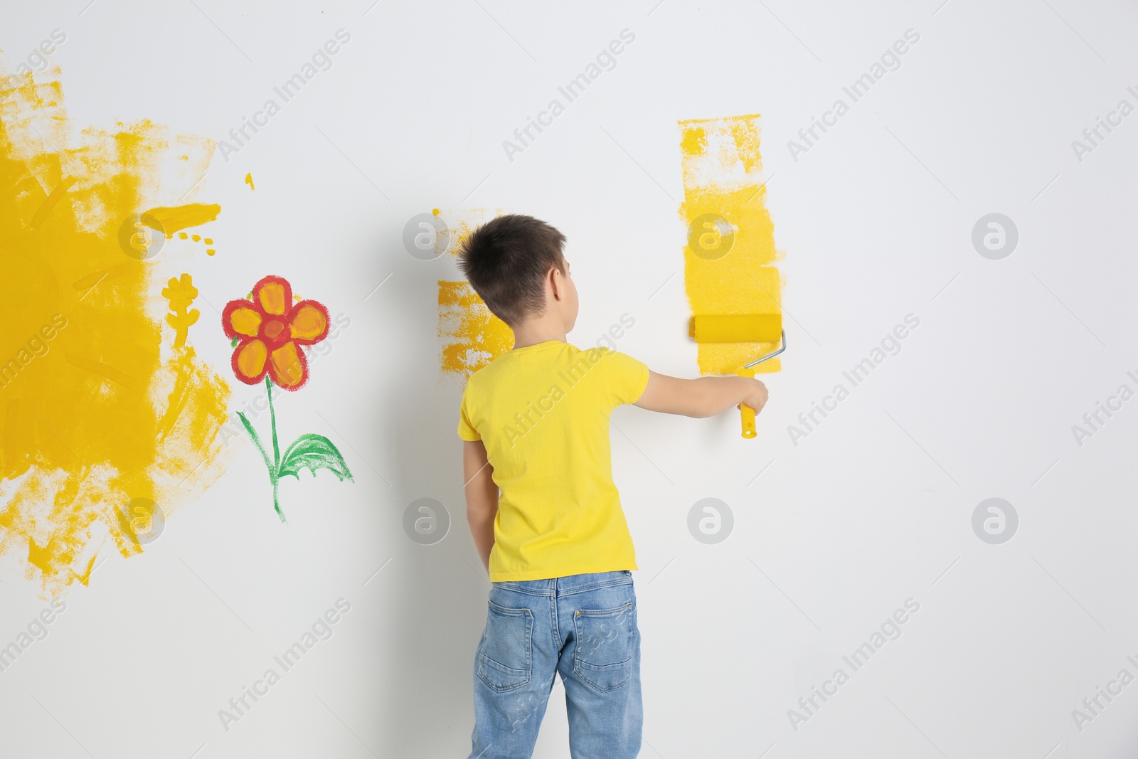 Photo of Little child painting wall with roller brush indoors