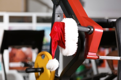 Photo of Santa Claus hat on modern exercise machine in gym