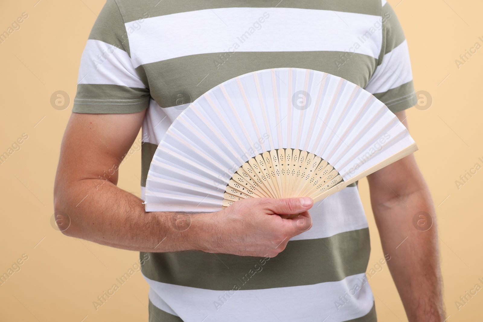 Photo of Man holding hand fan on beige background, closeup