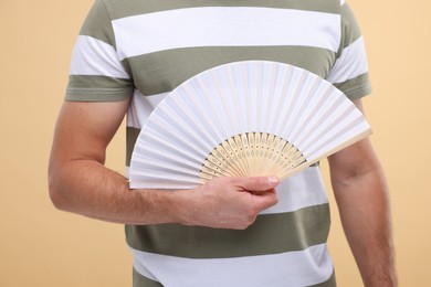 Man holding hand fan on beige background, closeup