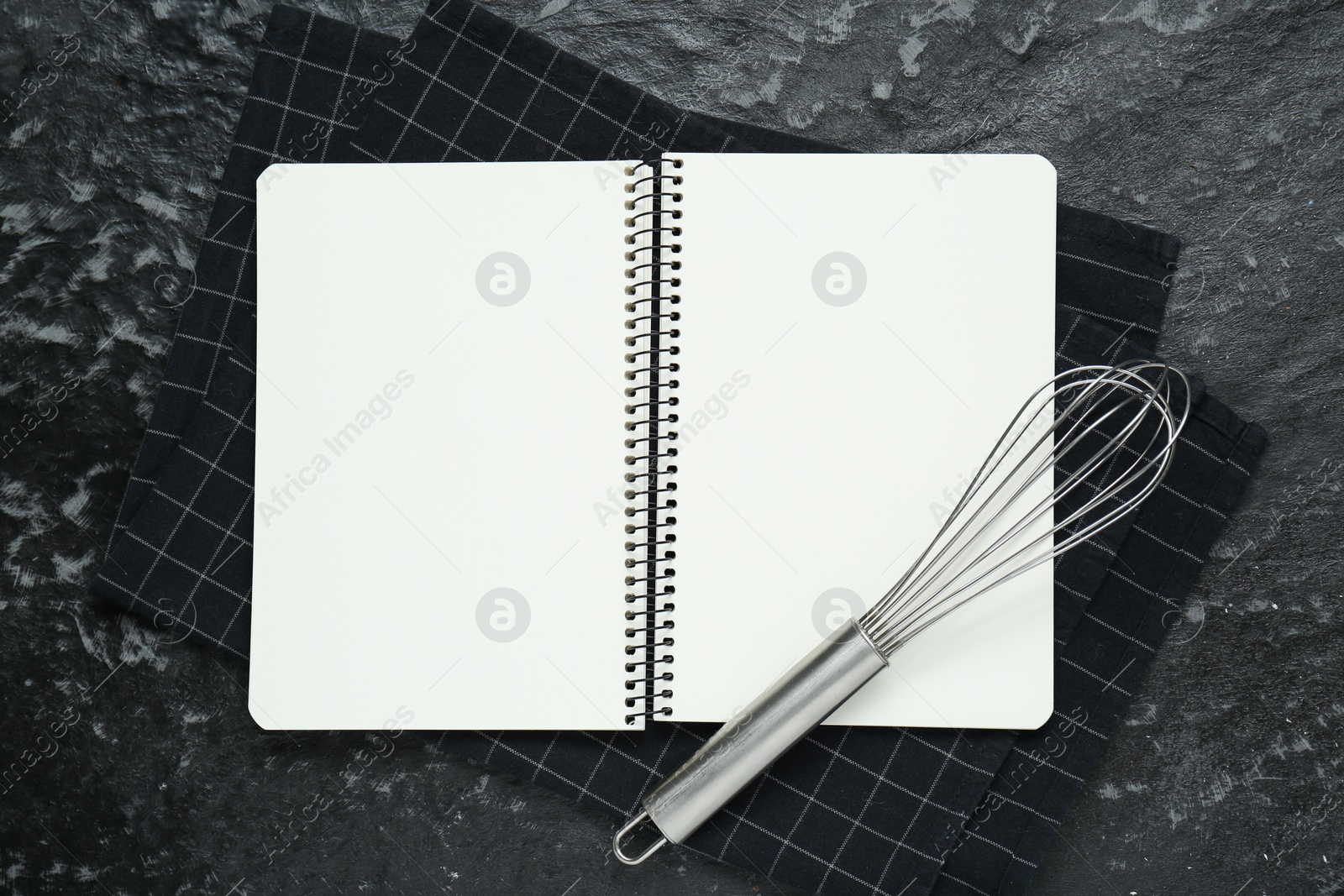 Photo of Blank recipe book and whisk on black textured table, flat lay. Space for text