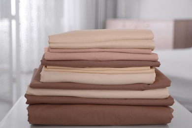 Photo of New clean folded bed linens on table indoors
