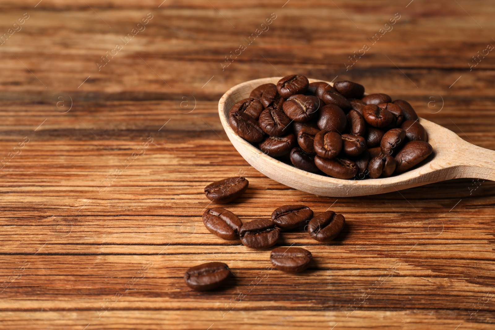 Photo of Roasted beans and spoon on wooden table, closeup. Space for text