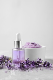 Photo of Natural cosmetic oil, bath salt, scrub and lavender flowers on grey marble table, space for text