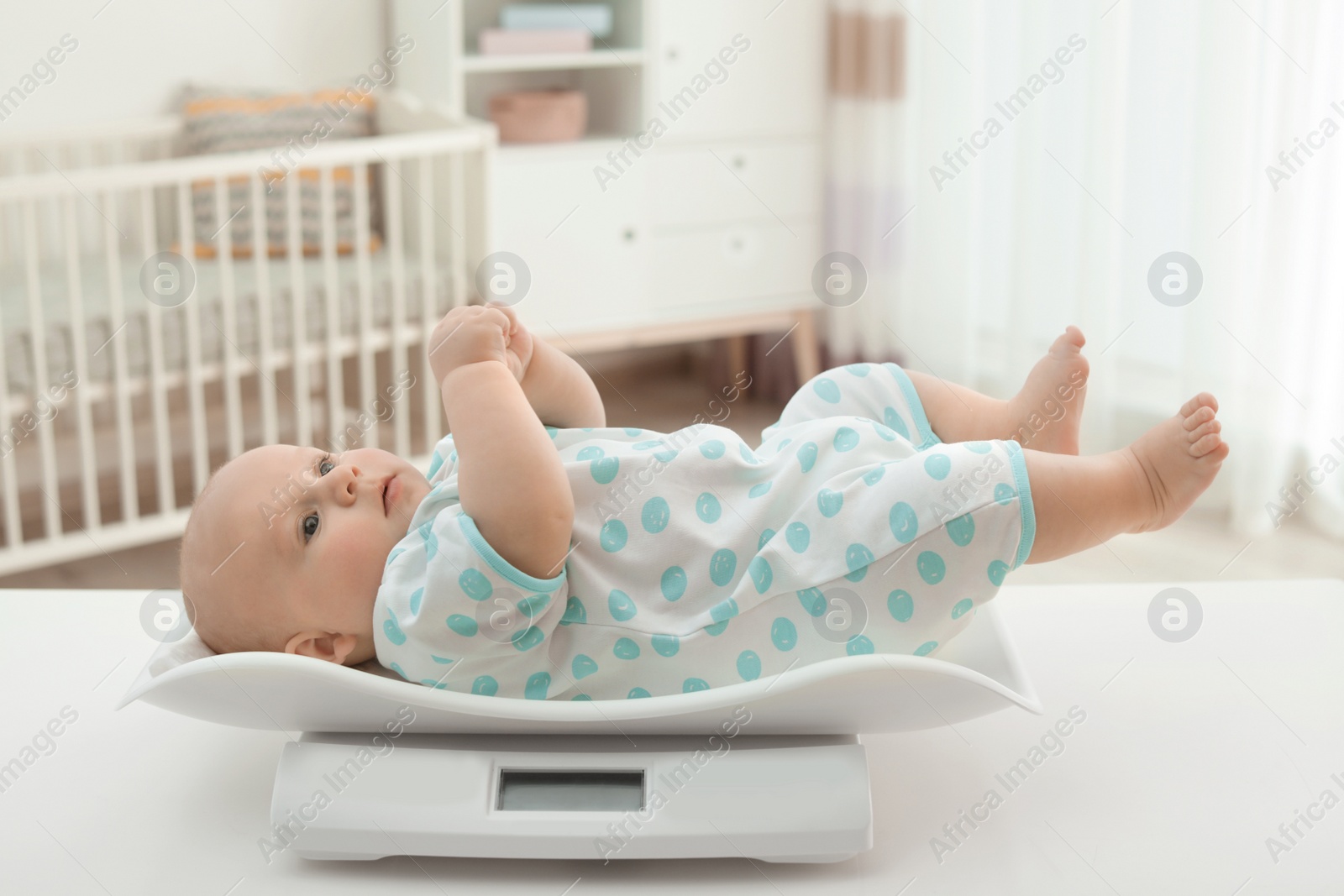 Photo of Cute little baby lying on scales in light room