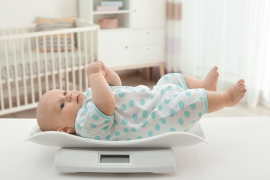 Photo of Cute little baby lying on scales in light room