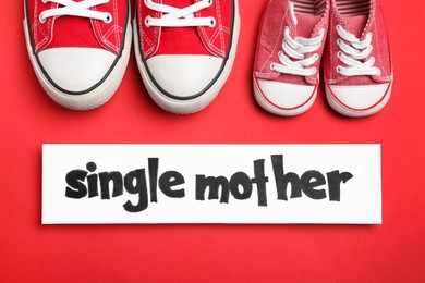 Photo of Being single mother concept. Children's and woman's gumshoes on red background, flat lay