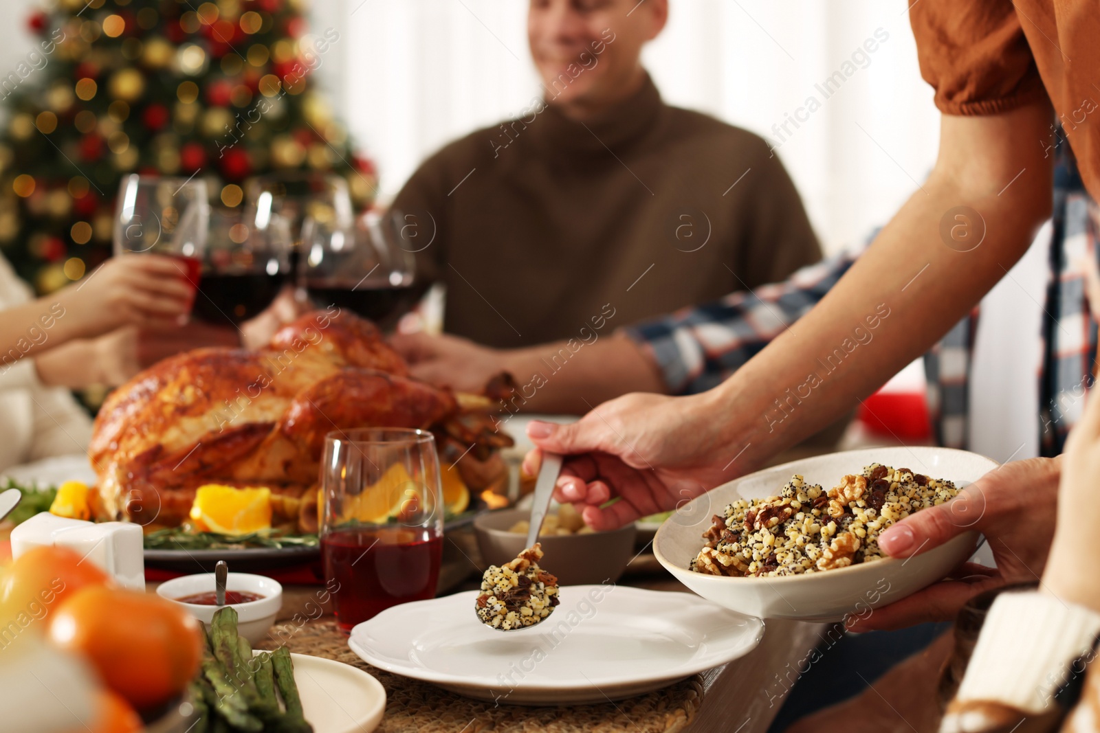 Photo of Mother putting traditional Christmas kutia onto her daughter's plate at festive dinner, closeup. Slavic dish