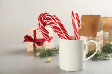 Photo of Christmas candy canes in cup on light grey table, space for text
