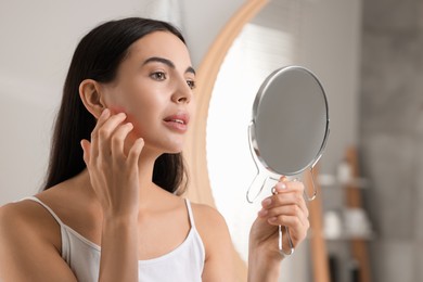 Photo of Suffering from allergy. Young woman looking in mirror and scratching her face indoors