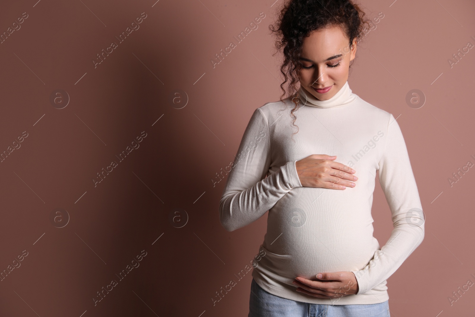 Photo of Pregnant young African-American woman on dusty rose background. Space for text