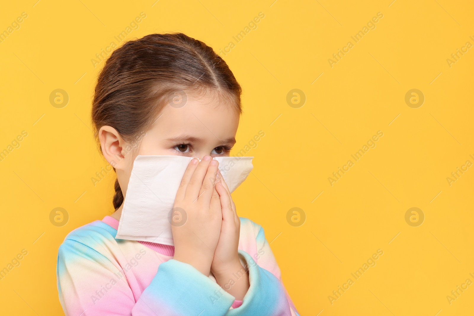 Photo of Girl blowing nose in tissue on orange background, space for text. Cold symptoms