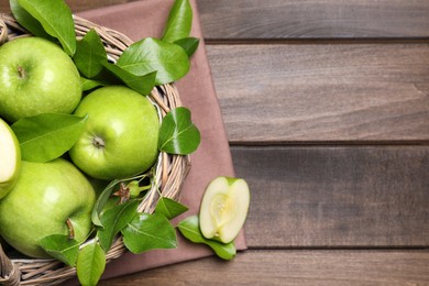 Photo of Fresh ripe green apples and leaves with wicker basket on wooden table, flat lay. Space for text