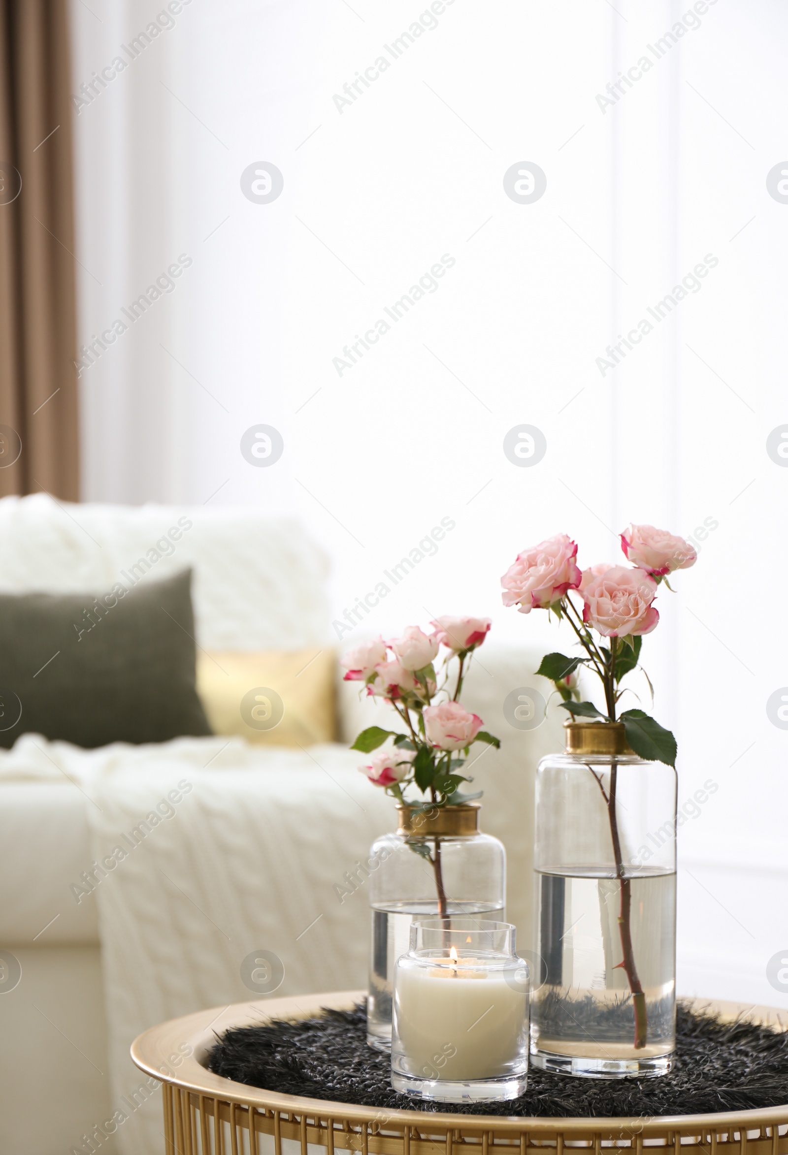 Photo of Burning candle and vases with beautiful roses on table indoors, space for text. Interior elements