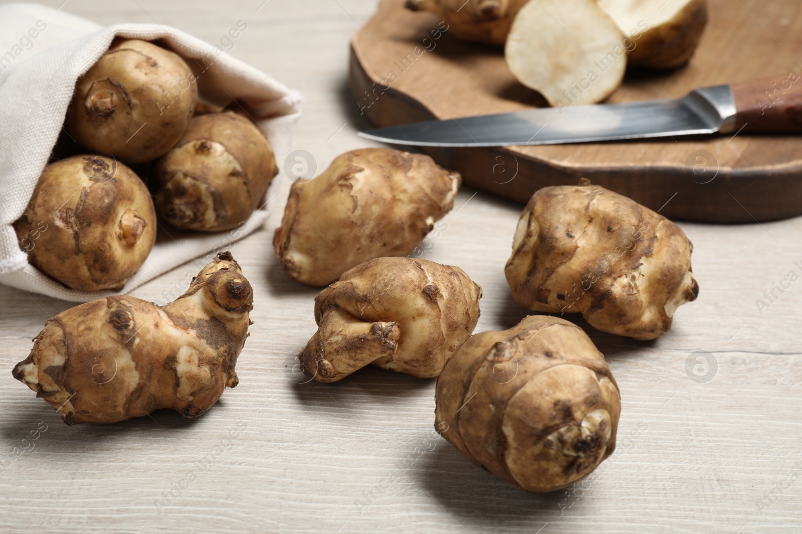 Photo of Bag and many Jerusalem artichokes with knife on white wooden table