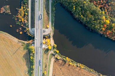 Image of Aerial view of road bridge across river near beautiful autumn forest