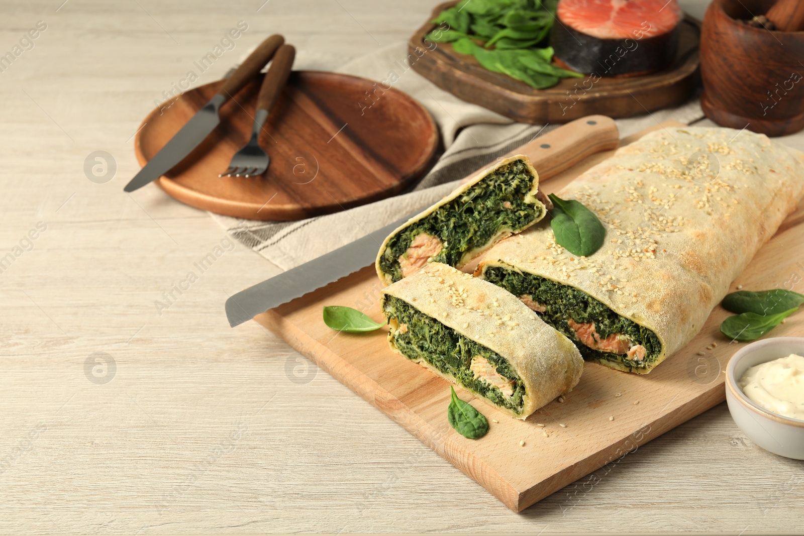 Photo of Delicious strudel with salmon and spinach served on light wooden table