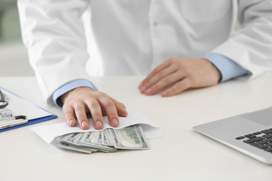 Photo of Doctor with bribe at desk in clinic, closeup. Corrupted medicine