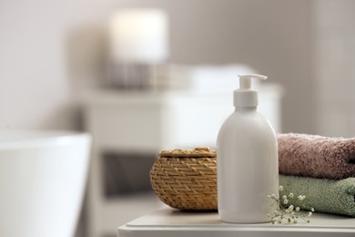 Photo of Bottle of bubble bath, towels, wicker box and flowers on white table in bathroom, space for text