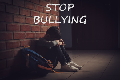 Image of Message STOP BULLYING and sad little boy sitting on floor near brick wall indoors