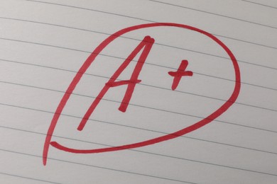 School grade. Red letter A with plus symbol on notebook paper, closeup