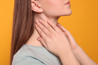 Woman with sore throat on orange background, closeup