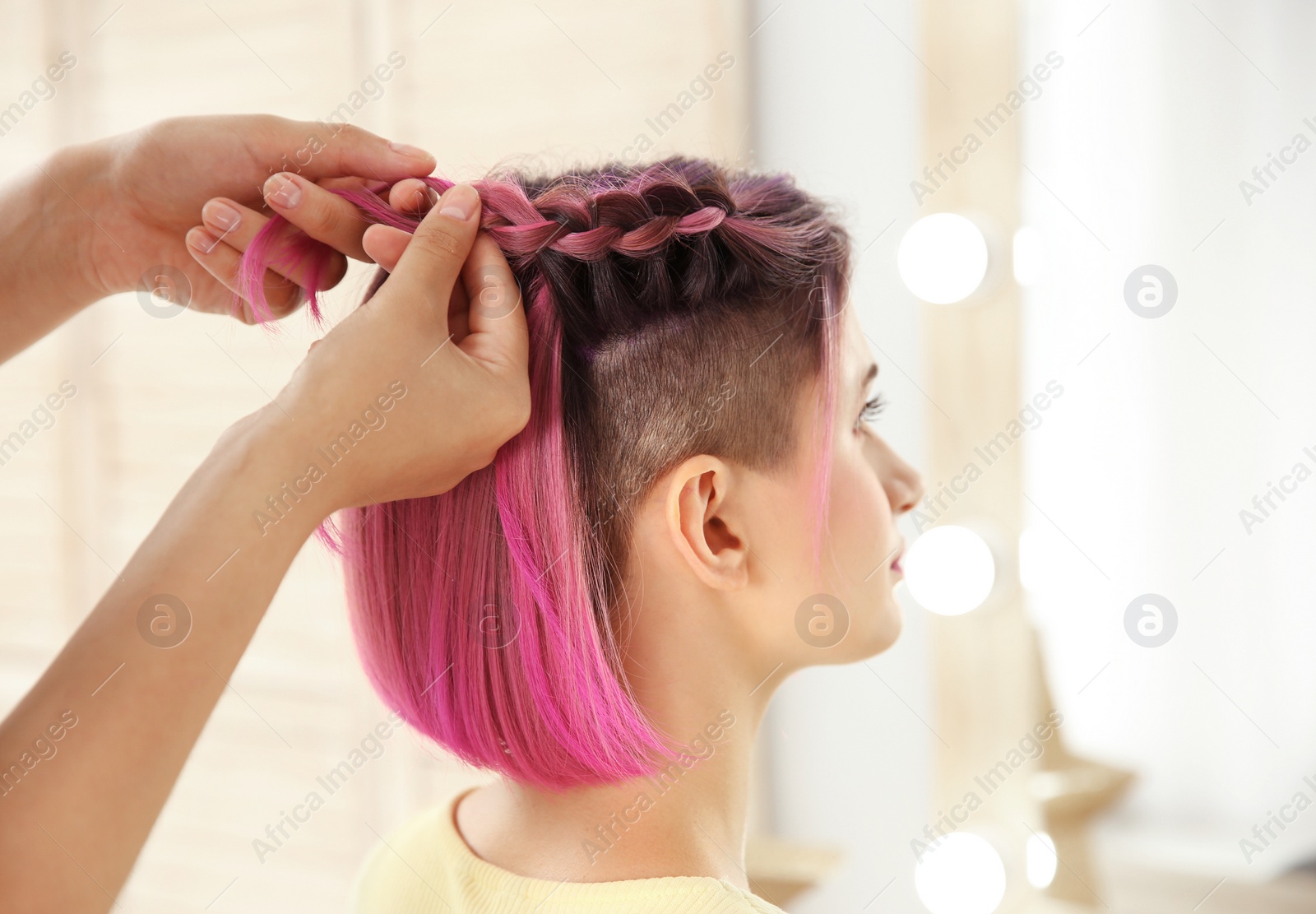 Photo of Professional stylist braiding woman's color hair in beauty salon. Modern trend