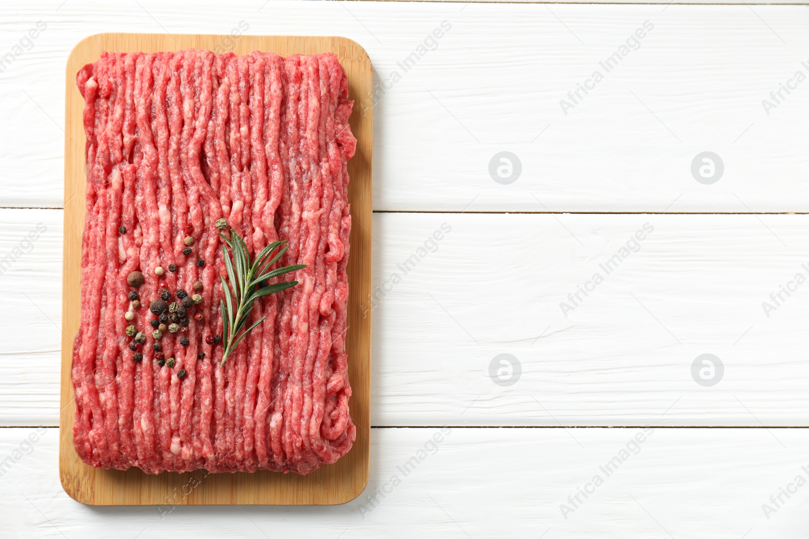 Photo of Raw ground meat, rosemary and peppercorns on white wooden table, top view. Space for text