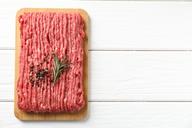 Photo of Raw ground meat, rosemary and peppercorns on white wooden table, top view. Space for text