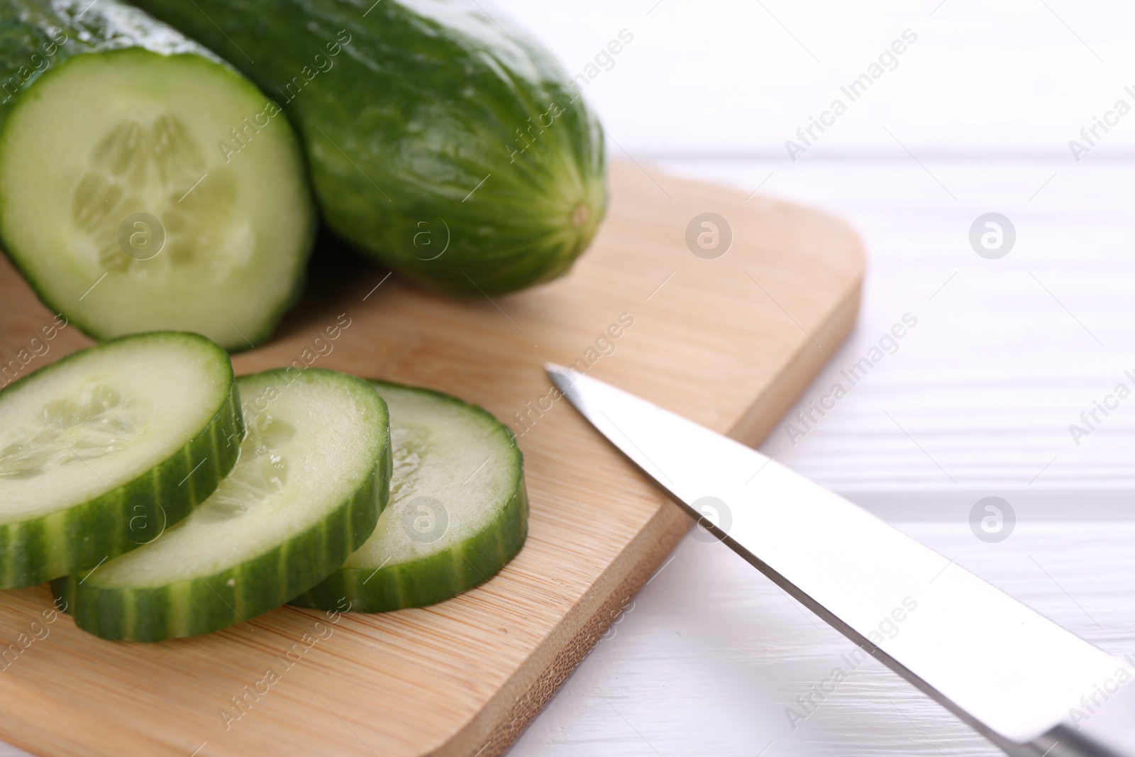 Photo of Cucumbers, knife and cutting board on white table, closeup