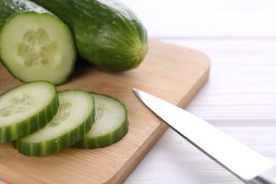 Cucumbers, knife and cutting board on white table, closeup