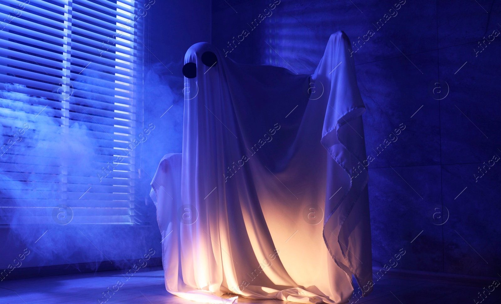 Photo of Creepy ghost. Woman covered with sheet near window in blue light