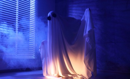 Photo of Creepy ghost. Woman covered with sheet near window in blue light