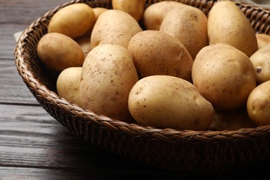 Photo of Raw fresh potatoes in wicker basket on wooden table, closeup