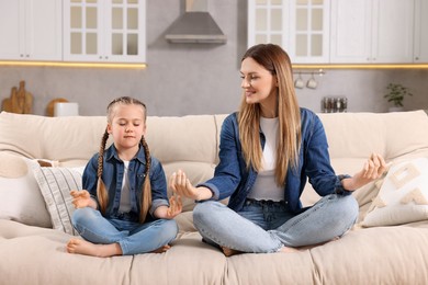 Photo of Mother with daughter meditating on sofa at home. Harmony and zen