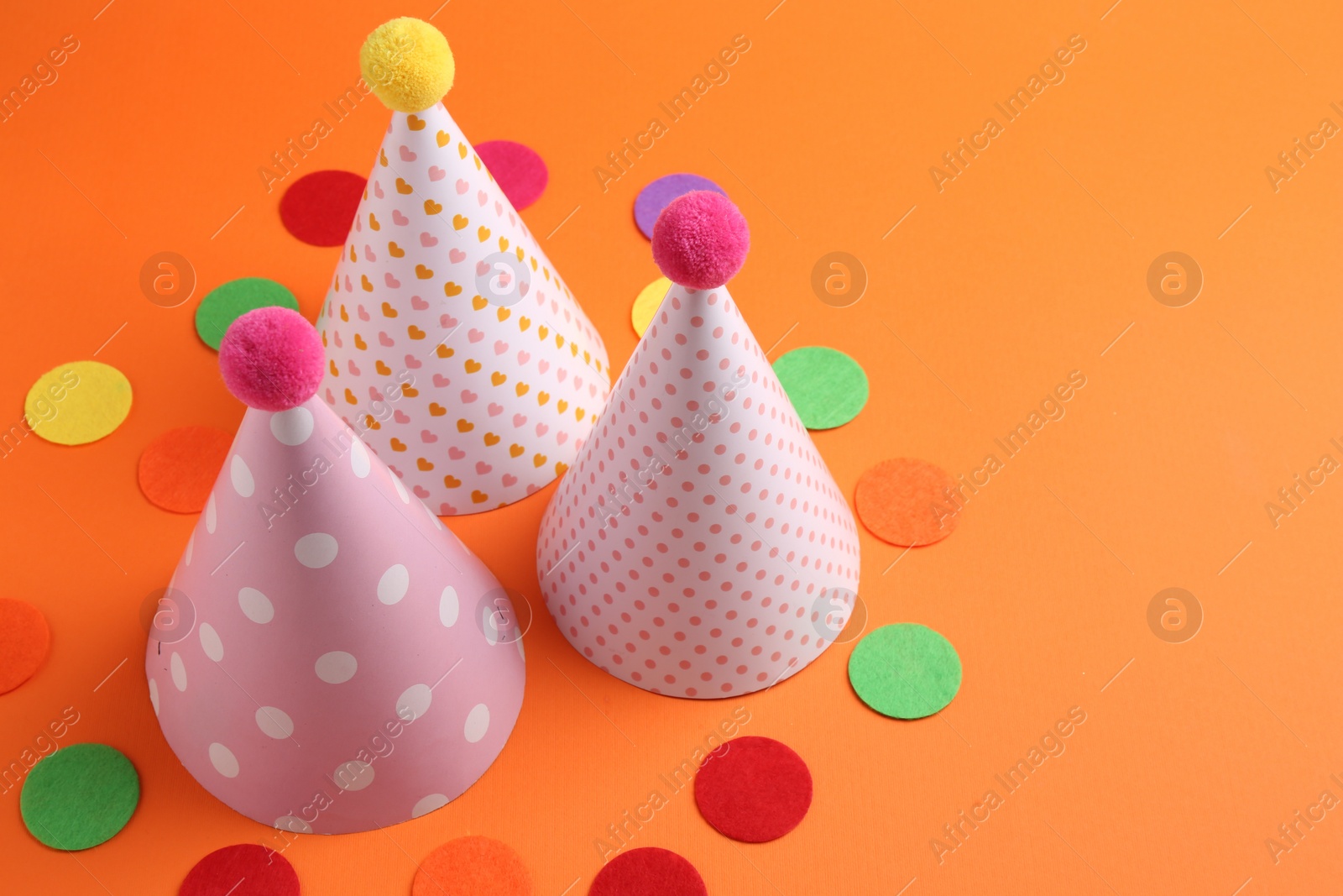 Photo of Party hats and colorful confetti on orange background. Space for text