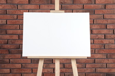 Photo of Wooden easel with blank canvas near brick wall