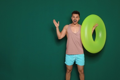 Funny young man with bright inflatable ring on dark green background, space for text