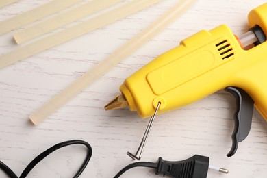 Photo of Yellow glue gun and sticks on white wooden table, flat lay