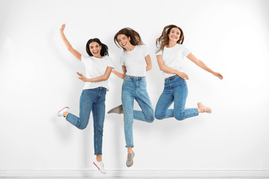 Photo of Group of young women in stylish jeans jumping near white wall