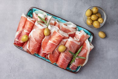 Photo of Rolled slices of delicious jamon with rosemary and olives on grey table, flat lay