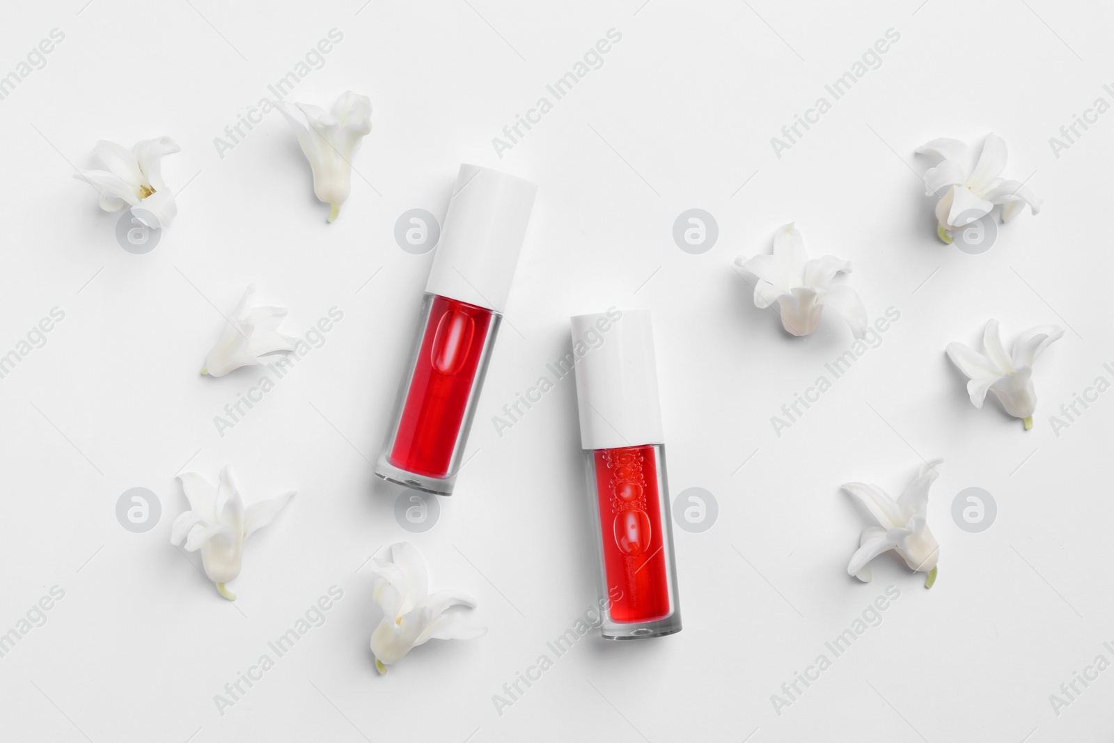 Photo of Bright lip glosses and flowers on white background, flat lay