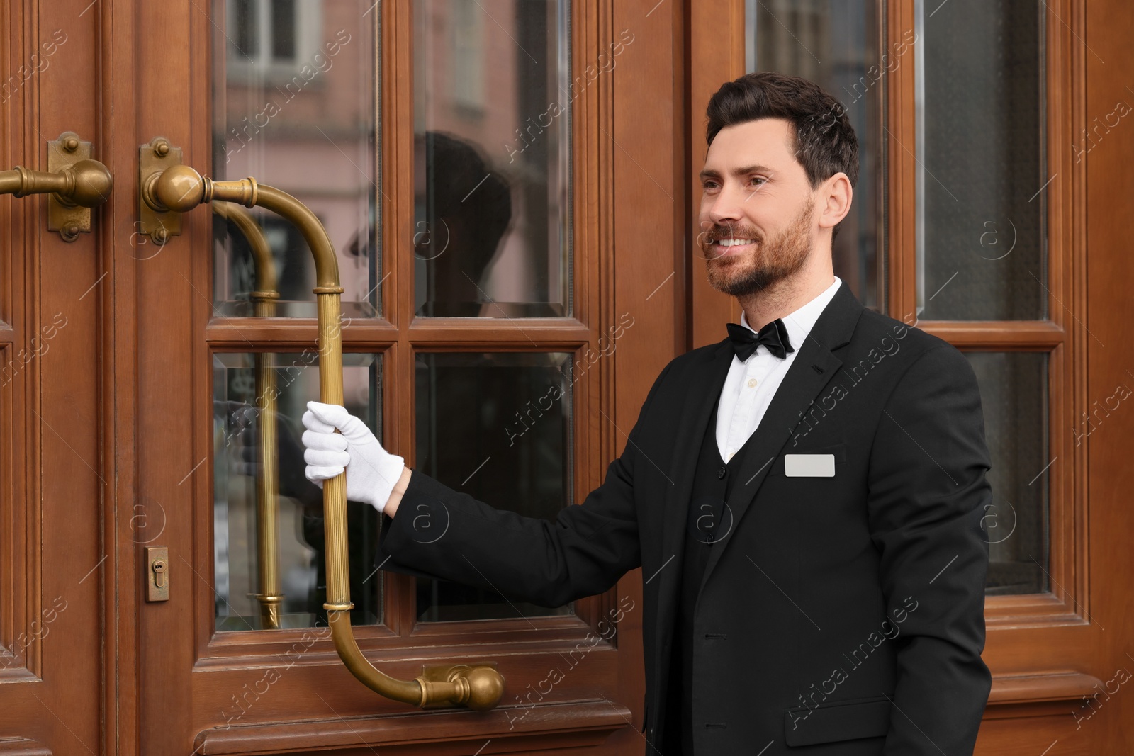 Photo of Butler in elegant suit and white gloves opening wooden hotel door