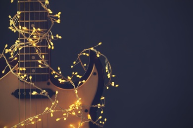 Photo of Guitar with festive lights on dark background, space for text. Christmas music