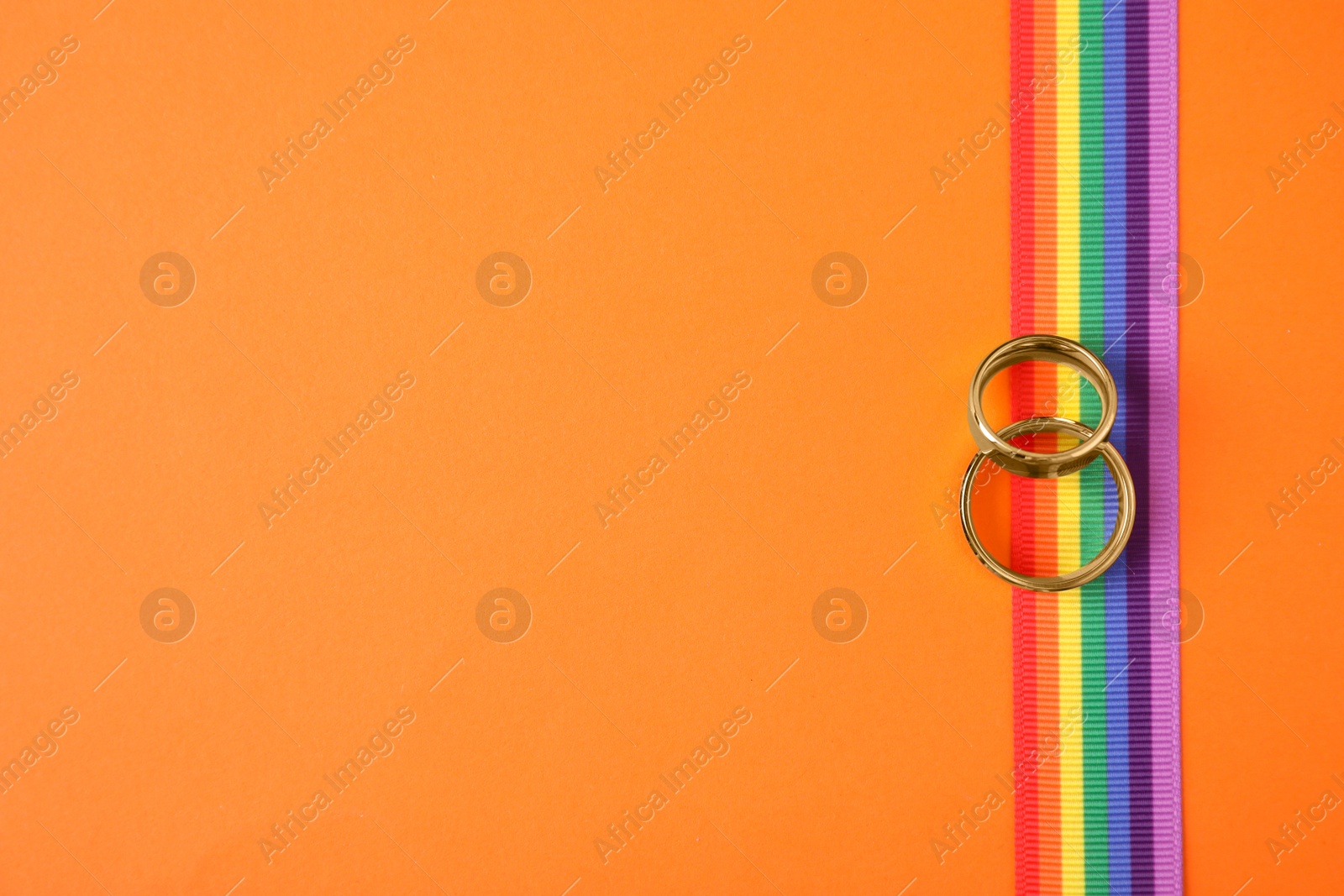 Photo of Top view of wedding rings and rainbow ribbon on color background, space for text. Gay symbol