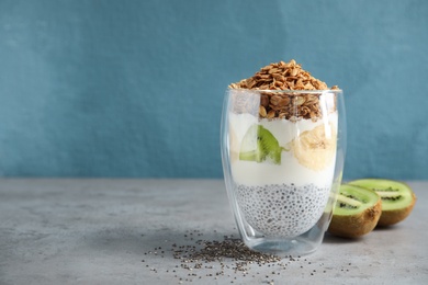 Photo of Glass of tasty chia seed pudding with granola and fruits on table. Space for text