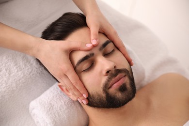 Photo of Young man receiving facial massage in beauty salon, above view